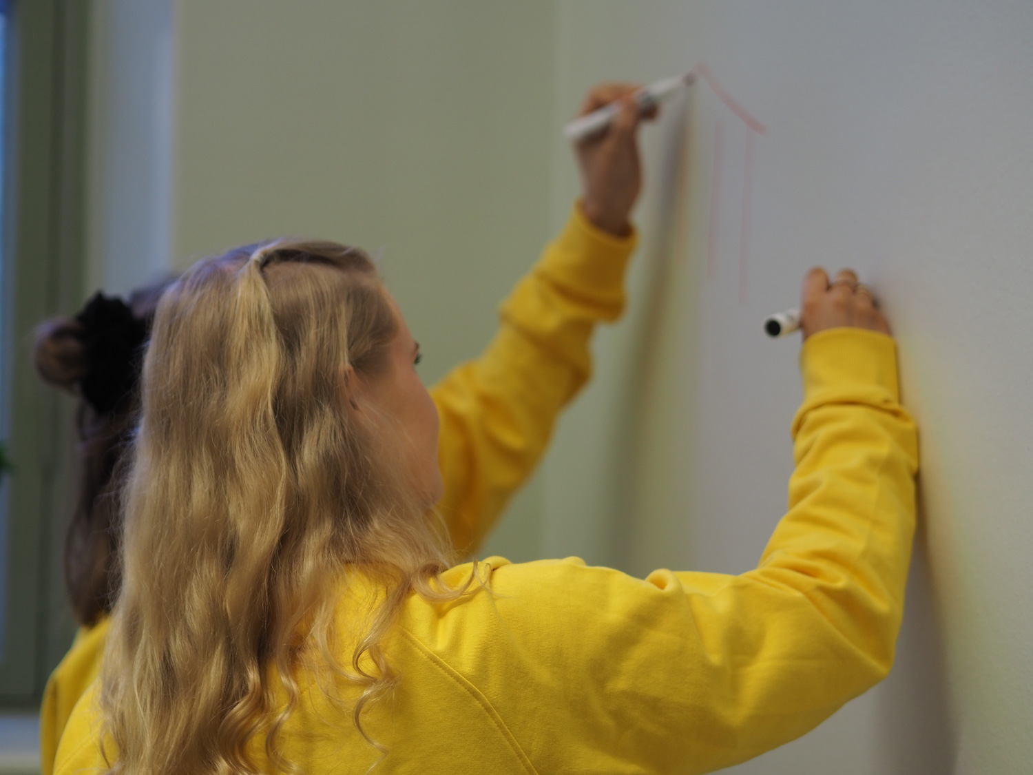 Kreetta Kiviniemi fotad bakifrån då hon ritar på en vit vägg.
